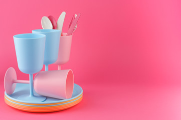 Colored plastic picnic utensils in bright colors. Glasses and plates in blue and pink. Eco dishes. Copy space.