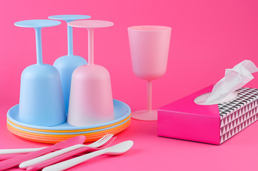 Colored plastic picnic utensils in bright colors. Glasses and plates in blue and pink. Copy space. Eco dishes in paper napkins.