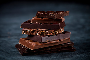 Chocolate bars pieces stack on black background. Sweet food photo concept.
