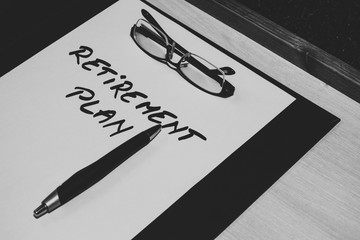 Sheet of paper with the message retirement plan handwritten on it, a pair of reading glasses and a pen placed on a clipboard &ndash; Concept image for money planning, and thinning about the future