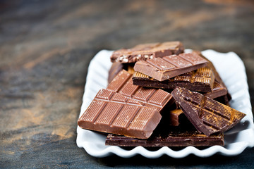 Chocolate bars pieces heap witn cinnamon powder on white ceramic plate.
