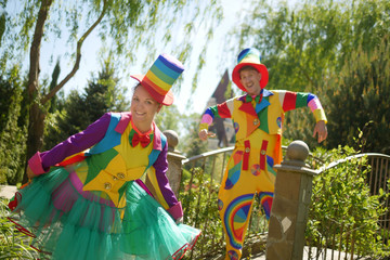 couple of funny clowns, a guy and a girl in a beautiful summer park, on a background of greenery