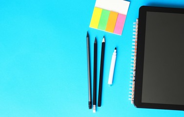 Pencils, writing paper and tablett on a blue background and back to school concept.