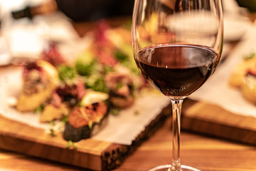 Red wine glasses on a wooden plank with defocused antipasto catering platter at the background