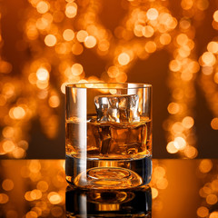 Glass of whiskey with ice cubes in front of christmas lights
