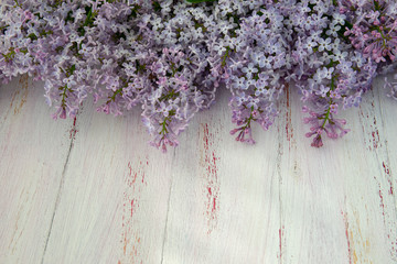 Frame of purple lilac and leaves on wooden background. Spring flowers. Decorative border, copy space, top view.