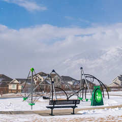 Square Playground and bench on a snowy playground against homes in winter