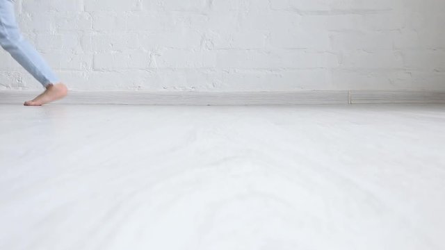 A child in jeans walks on the white floor. Feet close up.