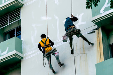 Two male workers are painting the outside of the tall building, By tying yourself to the rope, to job concept.