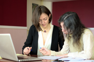 young smartly dressed lady helps another young lady to work with documents, fill forms and sign