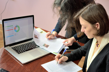 young smartly dressed lady helps another young lady to work with documents, fill forms and sign