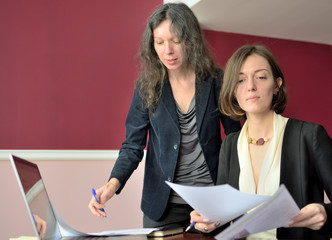 young smartly dressed lady helps another young lady to work with documents, fill forms and sign