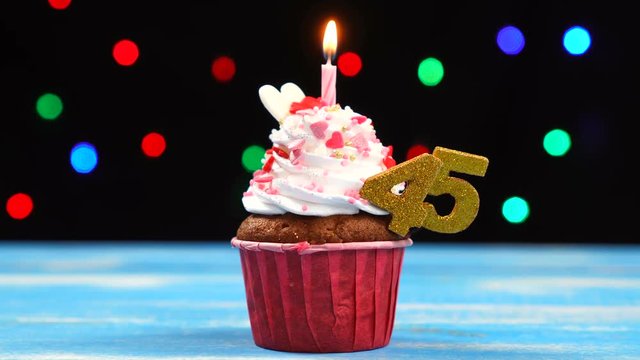 Delicious birthday cupcake with burning candle and number 45 on multicolored blurred lights background