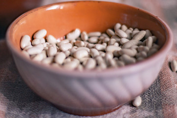 White beans in a clay deep plate on a linen tablecloth, soft focus