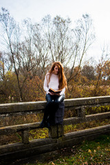 Portrait of young redhead woman in autumn park reading a book