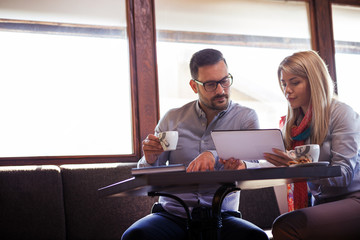 The handsome bearded boss looks very worried while watching the business results of the company on the tablet while sitting in a restaurant with his secretary.