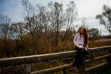 Naklejka na ściany i meble Portrait of young redhead woman in autumn park reading a book
