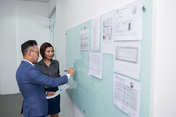 Businessman explaining to his partner the business strategy, he standing near the glass board and...