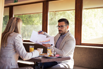 Young bearded handsome businessman with glasses shows business reports to his boss while dining at a restaurant.