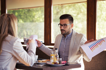 Young bearded handsome businessman with glasses shows business reports to his boss while dining at a restaurant.