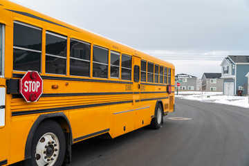Plakat Side view of a school bus on a road passing through snowy homes in winter
