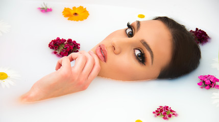 Obraz na płótnie Canvas attractive Caucasian model in milk bath with perfect teeth, face, skin and lips, and natural make up, beauty and spa concept with flowers and tropical leaves 