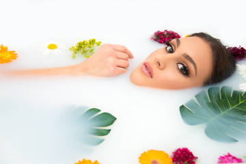 Obraz na płótnie Canvas attractive Caucasian model in milk bath with perfect teeth, face, skin and lips, and natural make up, beauty and spa concept with flowers and tropical leaves 