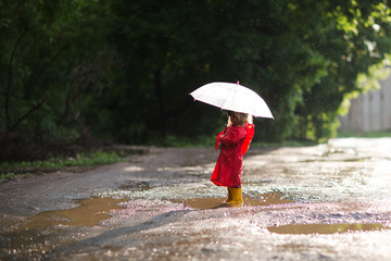 Happy child  with an umbrella playing out in the rain in the summer outdoors