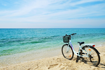 Fototapeta premium Feminine bicycle of comfort class with empty basket on the sandy beach of mediterranean sea. Blue cruiser bike on sunny day at sea shore with a lot of copy space for text.