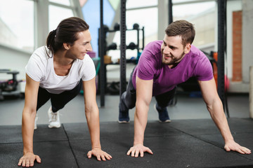 Obraz na płótnie Canvas Portrait of a muscular couple doing planking exercises in gym fitness health club. Together workout concept