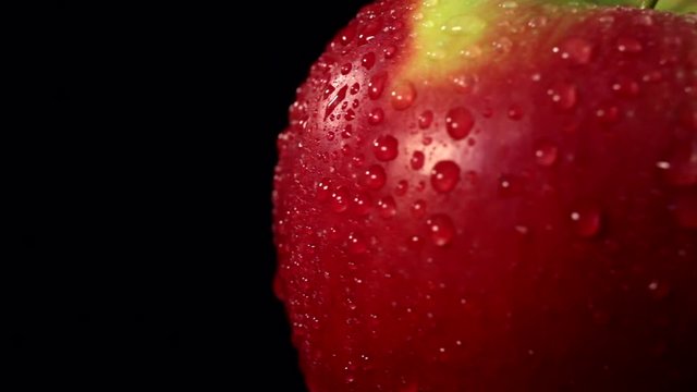 Red apple on a black background rotates around its axis. Closeup of an apple with water droplets.