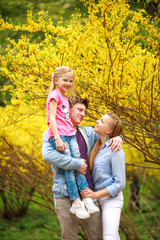 Fototapeta premium Young loving couple of parents with child daughter in park on background of yellow flowering tree