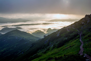 Fantastic view of mountain valley covered with low white puffy like snow clouds stretching to foggy...