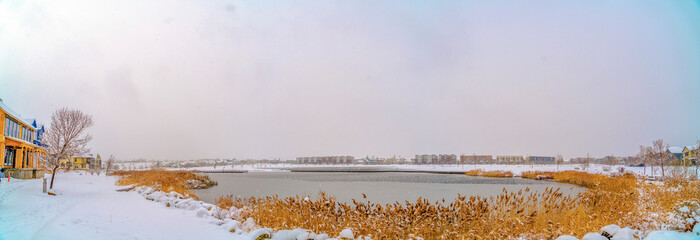Panorama of a lake in Daybreak with snow blanketing the grass lined shore