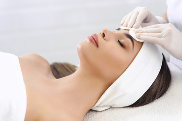 Close up of hands of skillful beautician cleaning and touching female face with cotton pad or...