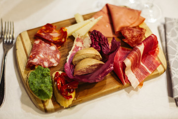 Table setting: white plates, rustic cloth with salami, cheese, vine, ham and wine bottle