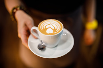 woman holding the cup of coffee latte with floral motif in the white milk foam