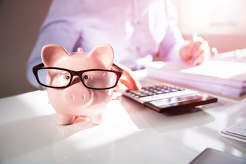 Businessman Calculating Invoice With Piggy Bank