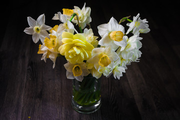 A bouquet of flowers on a dark wooden background. White narcissus in a vase. Place for your text. Top view.