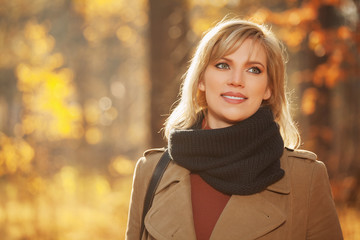 Happy young fashion woman in beige coat walking in autumn park