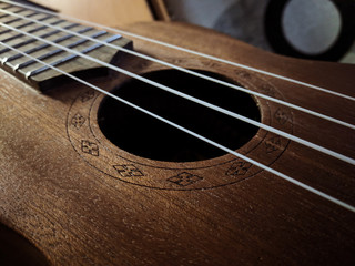 Obraz premium Defocused ukulele body, soundhole, bridge and neck on brown wooden background.