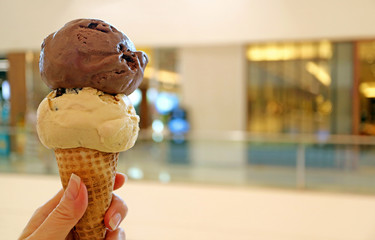 Female's hand holding ice cream cone with two scoops of chocolate and peanut butter icecream