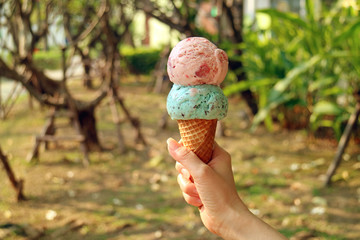 Two scoops of ice cream cone in woman's hand with blurry sunshine garden in background