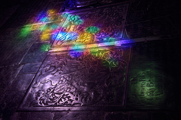 Stained glass colored light on carved tomb stone coat of arms on floor of Cordoba Cathedral Mosque