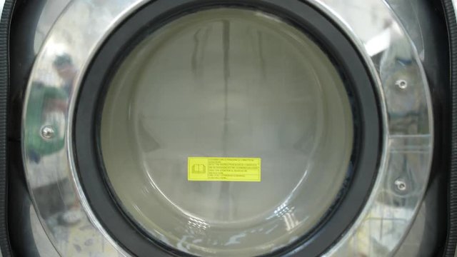 Spinning drum of loaded industrial washing machine in dry-cleaning salon, close-up on vibration of centrifuge. Big laundry machine spinning washed clothes after manual dry cleaning