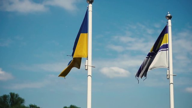 The national flag of Ukraine and the flag of the Ukrainian Navy against a blue sky. Slow motion. Close-up