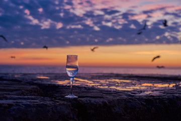 Romantic glass of wine sitting on the beach at colorful sunset Glasses of white wine against sunset, white wine on the sky background with clouds
