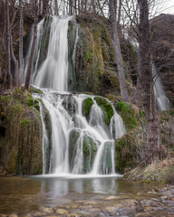 Obraz premium Long exposure view of a sunlit waterfall with soft streams of water falling down red rocks covered by green moss