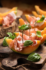 Sliced melon with ham and basil leaves, served on a wood chopping board
