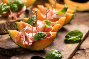 Sliced melon with ham and basil leaves, served on a wood chopping board